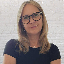 Eine Frau mit blonden Haaren und Brille, die in die Kamera schaut.