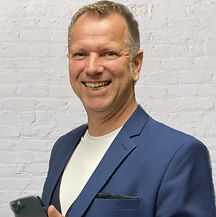 Mann in einem blauen Anzug hält ein Smartphone und lächelt in die Kamera.