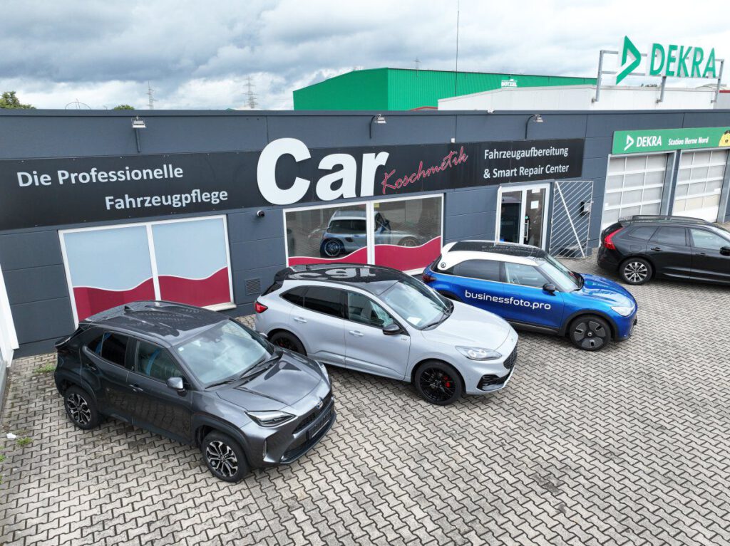 Drei Autos vor einem Fahrzeugreparaturzentrum mit dem Namen 'Car Xxschmiede'.